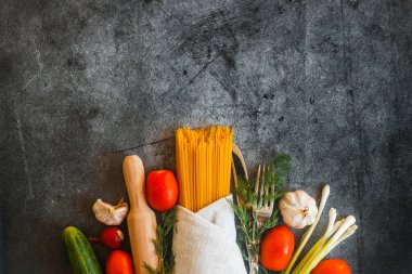 Beton zeminde sebzeler. Domates, salatalık, biber, turp, sarımsak, soğan, çimento bir masada otlar.