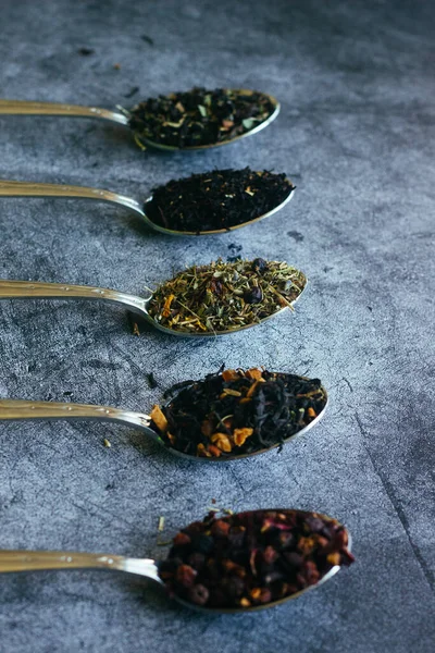 Various types of herbal tea in spoons. Spoons with dry tea leaves. Tea on a concrete background