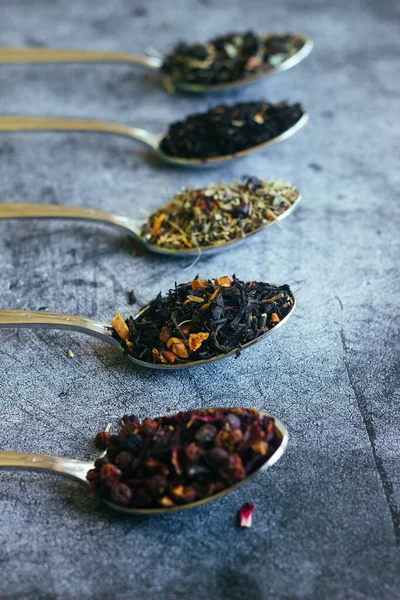 Various types of herbal tea in spoons. Spoons with dry tea leaves. Tea on a concrete background