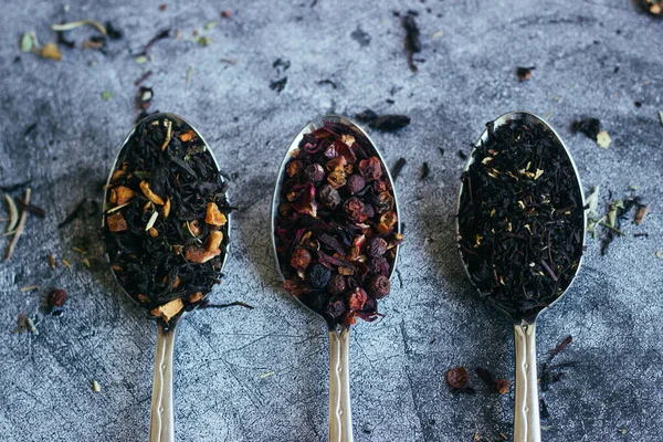 Various types of herbal tea in spoons. Spoons with dry tea leaves. Tea on a concrete background