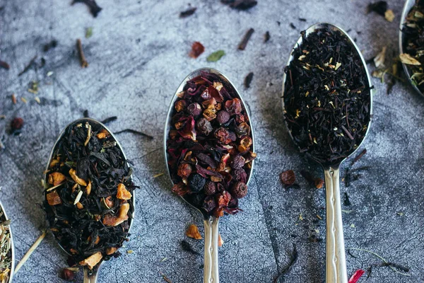 Various types of herbal tea in spoons. Spoons with dry tea leaves. Tea on a concrete background