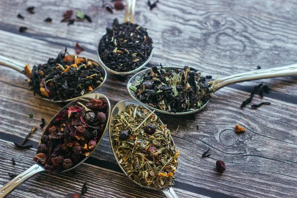 Various types of herbal tea in spoons. Spoons with dry tea leaves. Tea on a wooden background