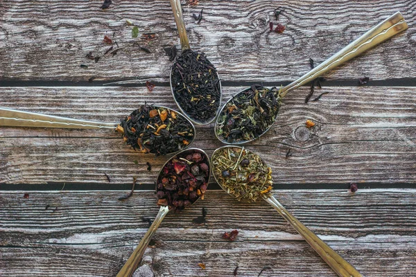 Various types of herbal tea in spoons. Spoons with dry tea leaves. Tea on a wooden background