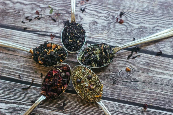 Various types of herbal tea in spoons. Spoons with dry tea leaves. Tea on a wooden background