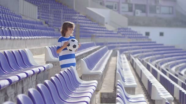小男孩足球运动员的慢动作与足球在体育场的看台上 — 图库视频影像