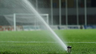 Futbol ya da futbol sahası sulama sistemi, otomatik sulama çimenleri. Futbol sahasını sulamak, dışarıdaki stadyumda kırmızı lastik yarış pistleri, 4K