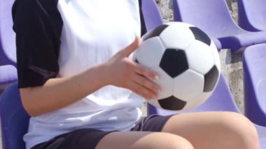 Stadyumda futbol topuyla oturan genç bayan futbolcu, 4K