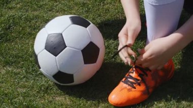 Futbol, futbol maçı. Profesyonel futbolcu genç bayan antrenmandan önce kırmızı ayakkabılarını bağlar, 4K