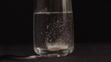Şişirilmiş C vitamini tableti siyah arkaplanda bir bardak suda köpürüyor, 75 fps yavaş çekim