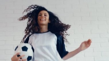 Futbol kıyafetli kıvırcık saçlı genç kadın atlıyor, 4K 75 fps yavaş çekim