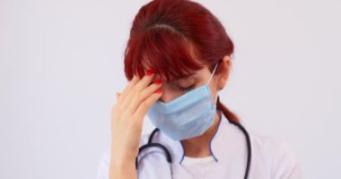 COVID-19 sağlık konsepti. Beyaz arka planda maskesi olan yorgun doktor kadının portresi. 4k ağır çekim