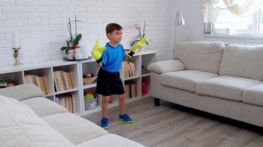 Karantina COVID-19 sırasında evde kaleci eldivenleriyle futbol oynayan altı yaşında bir çocuk. Dairesinde hayat devam ediyor. 4k