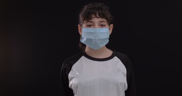 黒の背景に保護マスクとサッカーボールを持つ10代の女の子のサッカー選手の肖像 — ストック動画