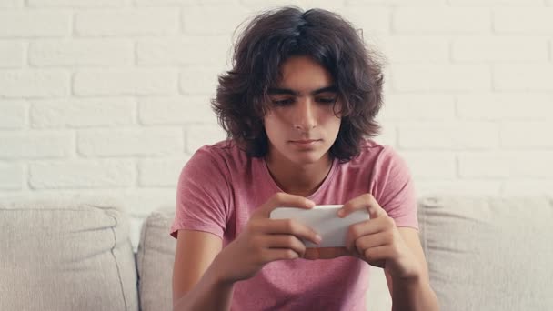 4K十代の男の子は自宅で彼の携帯電話で何かを見ている間に肯定的な反応を表現 — ストック動画
