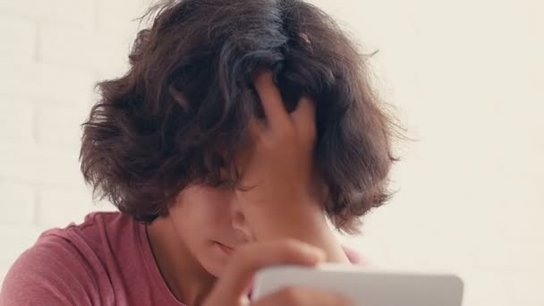 4K十代の少年は自宅で彼の携帯電話で何かを見ている間に否定的な反応を表現 — ストック動画