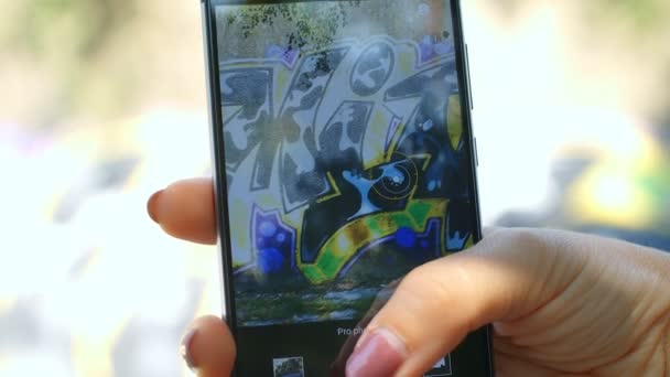 漂亮的高加索女孩 智能手机通过相机前 墙上有涂鸦的背景 慢动作75Fps — 图库视频影像