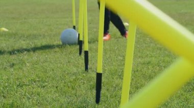 Futbol çeviklik eğitim ekipmanları. Futbolcu bacakları çeviklik direkleri arasında top sürüyor. 4k