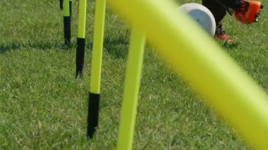 Futbol çeviklik eğitim ekipmanları. Futbolcu bacakları çeviklik direkleri arasında top sürüyor. 4k