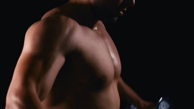 Daha büyük kaslar için halterleri kaldırıyorum. Büyük pazıları olan yakışıklı bir adam karanlık arka planda ağırlık kaldırıyor. 4k ağır çekim