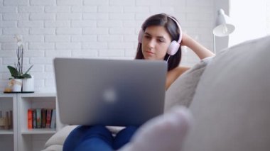 Kulaklıklı genç kadın laptopta çalışıyor evdeki kanepede oturuyor, 4 km ağır çekimde.