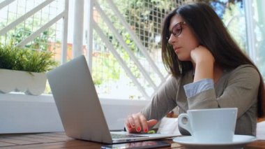 Güzel, başarılı bir iş kadını laptopuyla kafede kahve içiyor, dizüstü bilgisayarda çalışıyor ve telefon kullanıyor..