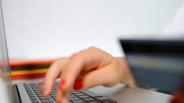 Kadının biri internetten bilgisayarlı kredi kartıyla alışveriş yapıyor. Eller, kredi kartı ve parmaklar klavyede.