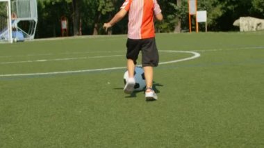 Futbol oynayan, futbol sahasında düşüp ağlayan küçük bir çocuğun kamera görüntüsü.