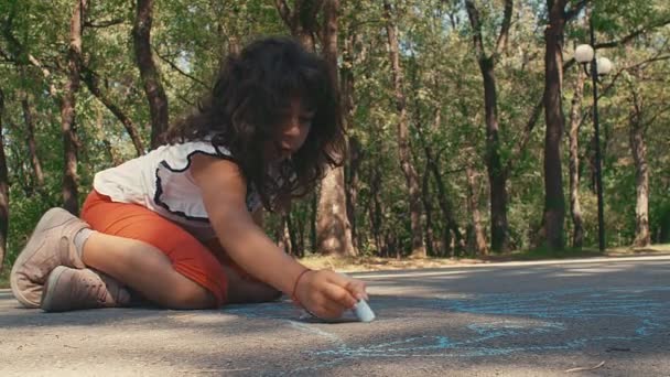 一个小女孩在沥青路面上画画 一个小女孩在公园里画粉笔 4K慢动作 — 图库视频影像