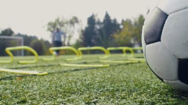 Futbol çeviklik eğitim ekipmanları. Top ile antrenman yapan oyuncu, ön çevik merdiven, engeller ve futbol topu. 4k ağır çekim