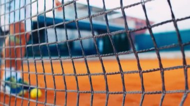 Tenis sahasının yanında raketle topu kaldıran bir adam var.