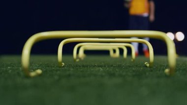 Geceleri elinde topla kameraya doğru ilerleyen bir futbolcu. Futbol çeviklik eğitim ekipmanları önde. 4k ağır çekim