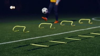 Futbolcu elinde topla, çeviklik antrenmanı ekipmanları gece ön tarafta. 4k ağır çekim