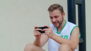 Basketbol Fan Reaction Concept - Basketbol kıyafetli heyecanlı basketbolcu akıllı telefondan en sevdiği takımı izliyor, 4K ağır çekim