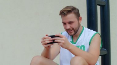 Basketbol Fan Reaction Concept - Basketbol kıyafetli heyecanlı basketbolcu akıllı telefondan en sevdiği takımı izliyor, 4K ağır çekim