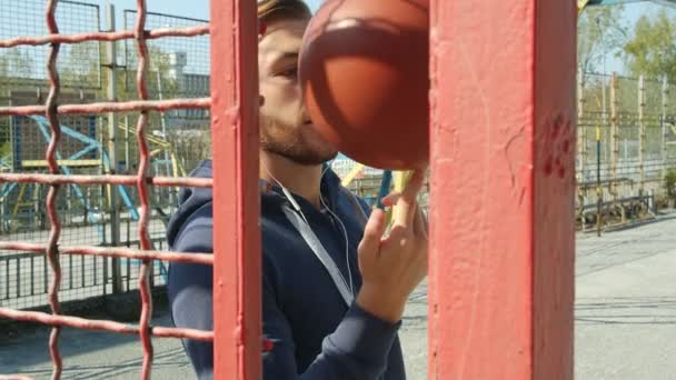 遊び場のネットの後ろにボールを回転バスケットボール選手の肖像画 彼の後にカメラ 4Kスローモーション — ストック動画