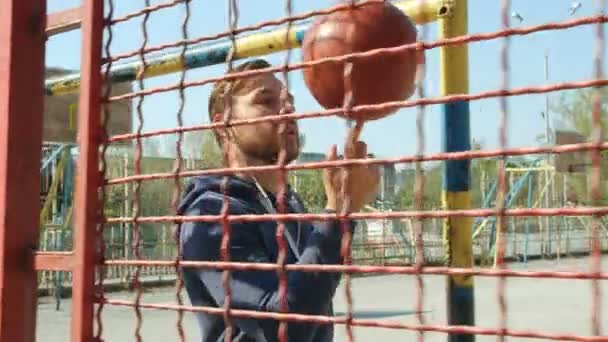 一个篮球运动员带着球在操场网后面行走的画像 摄像机跟着他 慢动作4K — 图库视频影像