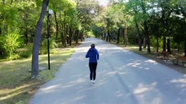 Sonbahar parkında koşan bir adamın İHA kamera görüntüsü, 4K