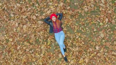 Sarı sonbahar yapraklarında uzanan güzel bir kadının hava manzarası. Kadın model, doğa arka planında hayatın tadını çıkarıyor. Kamera yakınlaştırılıyor. 4k ağır çekim
