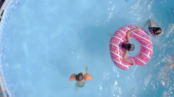 庭のスイミングプールで楽しんでいる幸せな小さな白人の子供たち 最上階だ 子供や子供のための涼しい夏の休日 水の上のゲーム ピンクのドーナツ — ストック動画