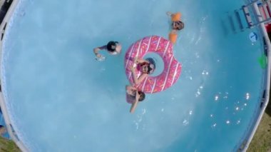 Küçük beyaz çocuklar bahçede yüzme havuzunda eğleniyorlardı. Üst Manzara. Çocuklar ve çocuklar için serin yaz tatilleri. Suda oyunlar. Pembe donat. 4k