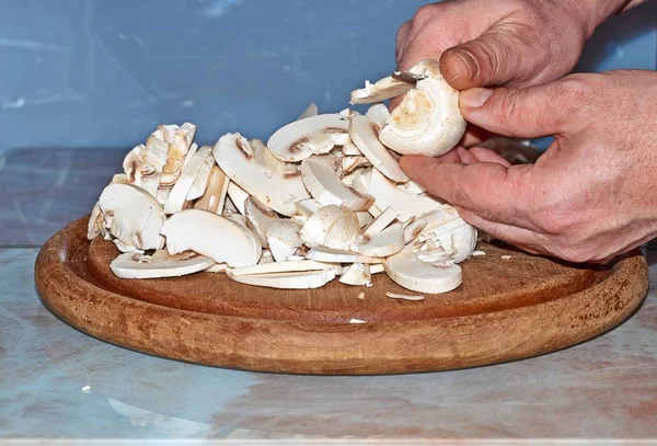 The chef cuts champignon mushrooms with vegetables. For cooking pizza, mushroom sauce, salad