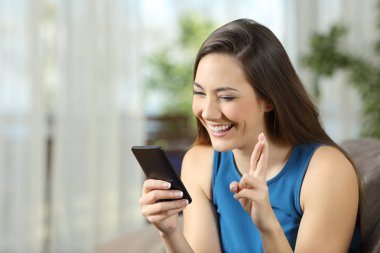 Oturma odasında evde bir kanepede oturan bir smartphone içinde online haber için bekleyen umutlu kadın 