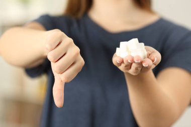 Front view close up of a woman hand holding sugar cubes with thumbs down at home clipart