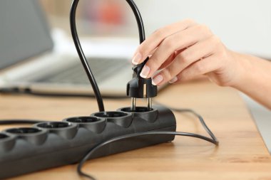 Close up of a woman hand plugging electric plug a in a socket on a table clipart
