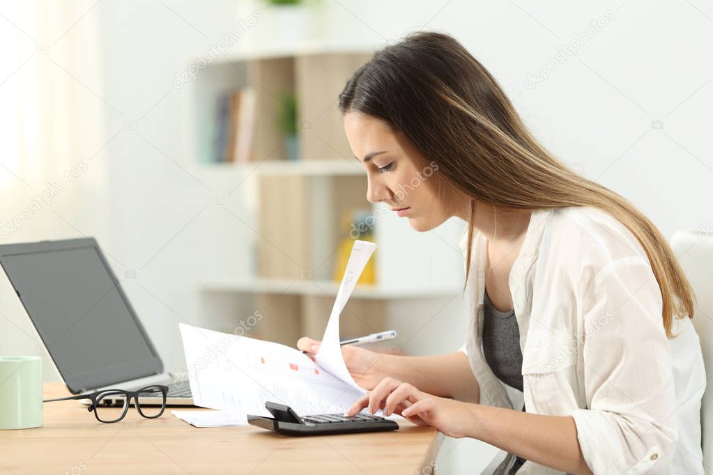 Side view portrait of a woman calculating expenses on a desktop at home