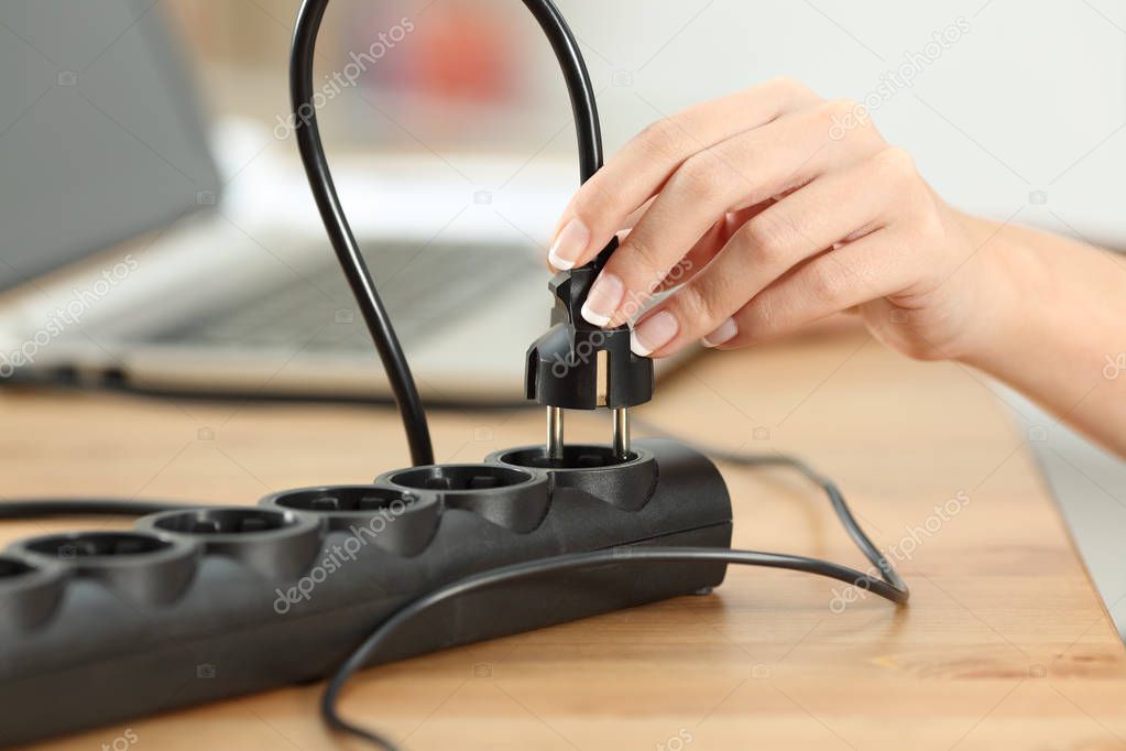 Close up of a woman hand plugging electric plug a in a socket on a table
