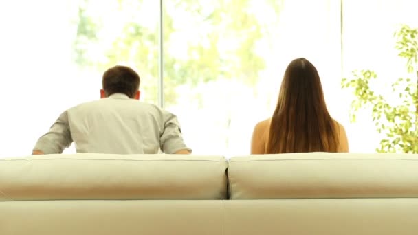 Rückansicht eines Paares, das es sich zu Hause auf einem Sofa gemütlich macht und durch das Wohnzimmerfenster aus einem grünen Hintergrund blickt