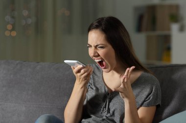 Oturma odasında evde bir kanepede oturan akıllı telefon, bağıran kızgın kadın