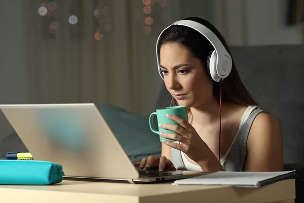 Student watching video tutorials holding a mug late hours in the night at home
