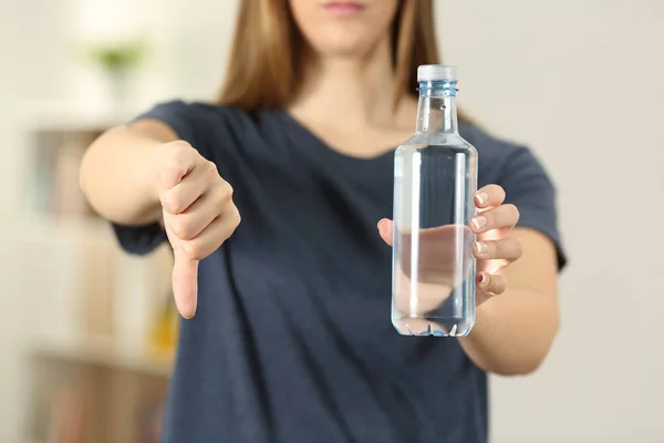前视图关闭一个女人手拿着一瓶水与拇指在家里 — 图库照片